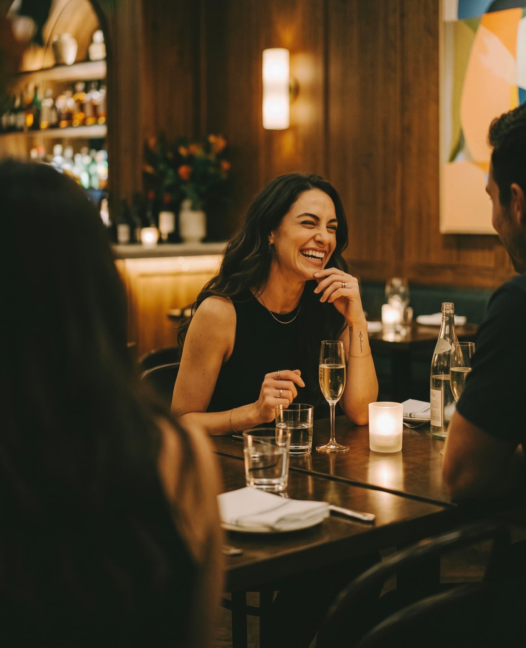 A woman laughing across a candlelit restaurant table